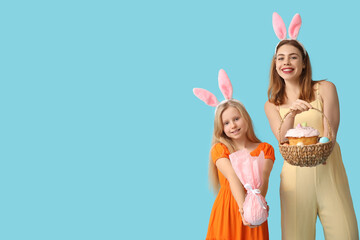 Poster - Cute little girl with gift egg and her mother in bunny ears holding basket with Easter cake on blue background