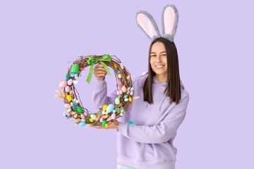 Sticker - Young woman in bunny ears with Easter wreath on lilac background