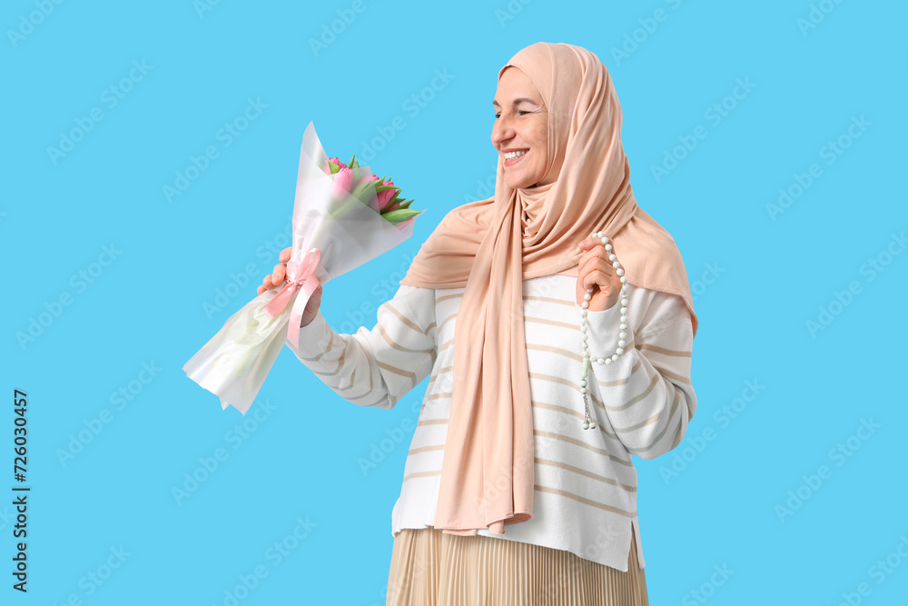 Mature Muslim woman with tulips on blue background. Ramadan celebration
