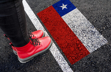 Wall Mural - a woman with a boots standing on asphalt next to flag of Chile and border
