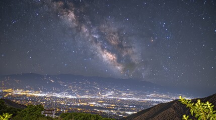 Milky Way Over Illuminated City and Mountainous Backdrop
