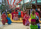 Fototapeta Młodzieżowe - a crowd of women in flamenco dresses through the narrow streets of the Feria of Seville