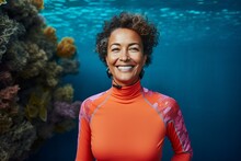 Portrait Of A Smiling Woman In An Orange Wetsuit Standing In Front Of A Coral Reef