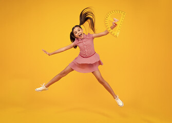 Poster - Amazed teenager. Measuring school equipment. Schoolgirl holding measure for geometry lesson, isolated on yellow background. Crazy jump, jumping kids. Student study math. Excited teen girl.