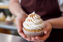 Closeup view of hands of female confectioner or baker holding fresh decorated cupcake with whipped cream top