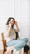 © Yauhen - Serious millennial woman talks on the phone, sitting on a chair and looking out the window in her free time. Serious pretty millennial woman calls by phone, talks, sits on chair, looks out window.