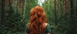 A woman with red hair admires the forest, her hair long and well-maintained, as she faces away from the camera.