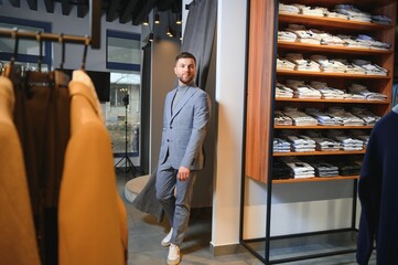 Wall Mural - Modern young handsome businessman, looking and choosing classical suit in the suit shop