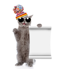 Poster - Happy cat wearing sunglasses and knitted warm woolen hat with pompon shows blank list. isolated on white background