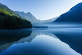 Fototapeta Do pokoju - A serene alpine lake at dawn, with mist rising off the water and mountains reflected in the still surface