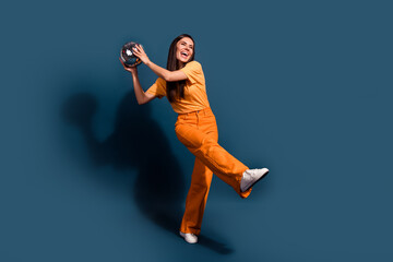 Poster - Full body length photo of lady wear orange t shirt and pants hold shining disco ball at home party isolated on dark blue color background