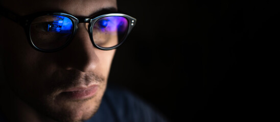 Portrait of a young male programmer wearing computer glasses with blue highlights on a black background with copy space.