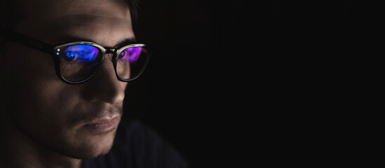 portrait of a young male programmer wearing computer glasses with blue highlights on a black backgro