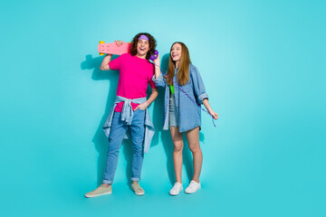 Wall Mural - Full body photo of young couple teenagers boyfriend with girlfriend hobby penny board talking old phone isolated on cyan color background