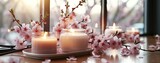 Fototapeta Uliczki - Scented candles and pale pink cherry blossom on table, window in background