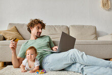 Cheerful Man Holding Credit Card While Doing Online Shopping Near Baby Boy On Carpet With Rattle