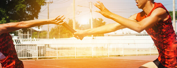 Wall Mural - Professional Athlete passing a baton to the partner against race on racetrack.selective focus.