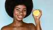 Skin care organic cosmetic concept. Beauty portrait of Overjoyed African american model holding a fresh lemon, posing against blue background.