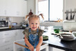 © Austockphoto - Happy toddler girl standing in messy kitchen with dishes piled on bench