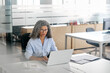 © insta_photos - Busy mature middle aged professional business woman, older lady manager executive leader looking at laptop using computer in office working on digital project sitting at desk. View through glass.