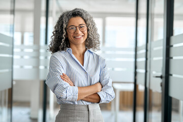 Smiling happy confident old mature professional business woman corporate leader, senior middle aged female executive, lady bank manager standing in office arms crossed looking at camera, portrait.