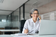 © insta_photos - Smiling middle aged mature business woman having conversation with customer talking on mobile phone in office making corporate call on smartphone using laptop computer working sitting at desk.