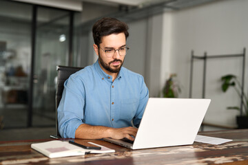Busy professional business man company employee, young male worker software developer, latin businessman typing on computer technology using laptop searching on web working at office workplace desk.