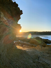 Wall Mural - Sunrise on a beach behind a rock. Dawn on the beach. Ocean view at low tide. Yellow mountains near the water. Beach at sunset.