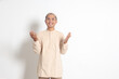 Portrait of religious Asian muslim man in koko shirt with skullcap praying earnestly with his hands raised. Devout faith concept. Isolated image on white background