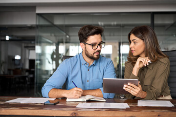 Busy colleagues working with digital tablet talking in office. Professional partners having conversation at meeting. Female executive manager showing work plan using tab helping new employee.
