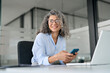 © insta_photos - Happy mature business woman executive holding mobile cell phone looking away in office. Smiling middle aged professional businesswoman manager wearing glasses using cellphone working on smartphone.