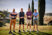 Sotogrante, Spain - January 26, 2024 - Four Male Golfers With Clubs, Lined Up And Smiling On A Golf Course, With Cypress Trees And A Clear Sky In The Background.