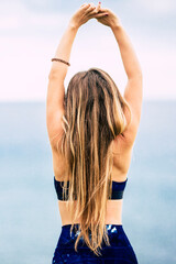 Wall Mural - Healthy lifestyle people concept with beautiful long blonde hair girl viewed from back do some stretching in front of the ocean view outdoor - fit woman and attractive female