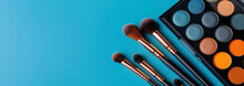 Colorful eyeshadow palette and professional makeup brushes on a blue background. Beauty and makeup concept with copy space for cosmetics design and tutorials.