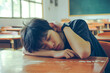 Bored asian student sleeping on his desk in the school classroom while holding his head with his hand