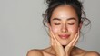 © buraratn - Portrait of beautiful asain woman touching her clean and healthy face against grey background Smiling hispanic woman with natural makeup feeling healthy skin with eyes closed Beauty care pampering