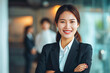 Portrait of a attractive smiling asian businesswoman in a suit standing in a modern business company office, with her workers standing in the blurry background