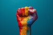 A raised fist painted with the pride rainbow on a colored background.