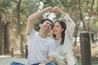 © kamiphotos - Happy young Asian couple in a park, Portrait of smiling couple near beautiful nature outdoors, lifestyle, Cheerful couple hugging each other, Young couple enjoying the sunny day at park