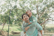 © kamiphotos - Happy young Asian couple in a park, Portrait of smiling couple near beautiful nature outdoors, lifestyle, Cheerful couple hugging each other, Young couple enjoying the sunny day at park