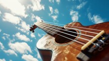 Close-Up View Of A Brown Acoustic Guitar With Strings, Tuning Pegs Against A Bright Blue Sky With Clouds - Musical Instrument Concept