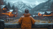 A Boy In A Yellow Raincoat Stands On A Wooden Fence And Looks At The Snow-covered Mountains. - Generative AI
