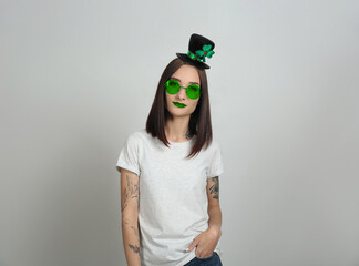 St. Patrick's day party. Pretty woman in leprechaun hat and green sunglasses on light grey background