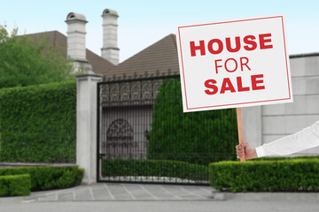 Sticker - House for sale. Woman holding signboard near beautiful house outdoors, closeup