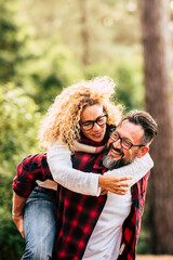 Wall Mural - Happy adult caucasian couple in relationship and love play together in the forest wood nature - outdoor people leisure activity concept with cheerful caucasians