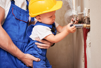 Wall Mural - Close up of male plumber holding little boy while child installing plumbing pipes in apartment under renovation. Father and son in safety helmet working on installation of sanitary equipment at home.