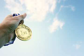 Wall Mural - man hand raised, holding gold medal against sky. award and victory concept