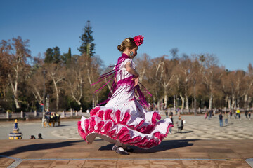 Girl dancing flamenco, twirling to show off her costume, in typical flamenco dress on a bridge in a beautiful square in Seville. Dance concept, flamenco, typical Spanish, Seville, Spain.