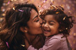 An affectionate young mother of Indian ethnicity kisses her little daughter on her birthday