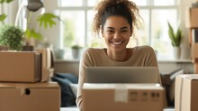 A Smiling Female Entrepreneur Is Sitting At A Table With A Laptop And Cardboard Boxes - The Concept Of A Small Business And Enterprise, Sales Via The Internet And An Online Store